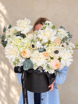 Woman holding Ivory Serenade white flower arrangement in a black hat box
