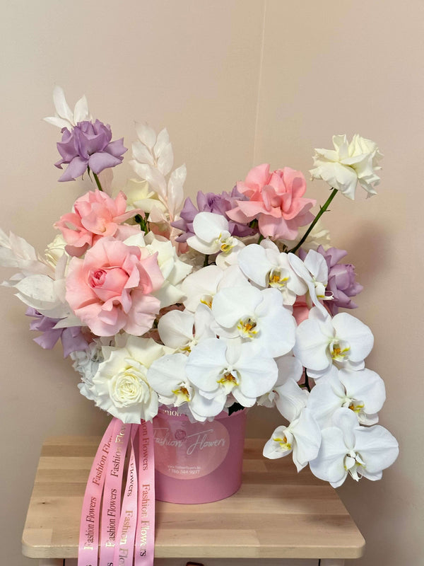 Ángel de ensueño: caja con rosas rosadas, blancas y violetas, hortensias, orquídeas blancas y decoración de moda.